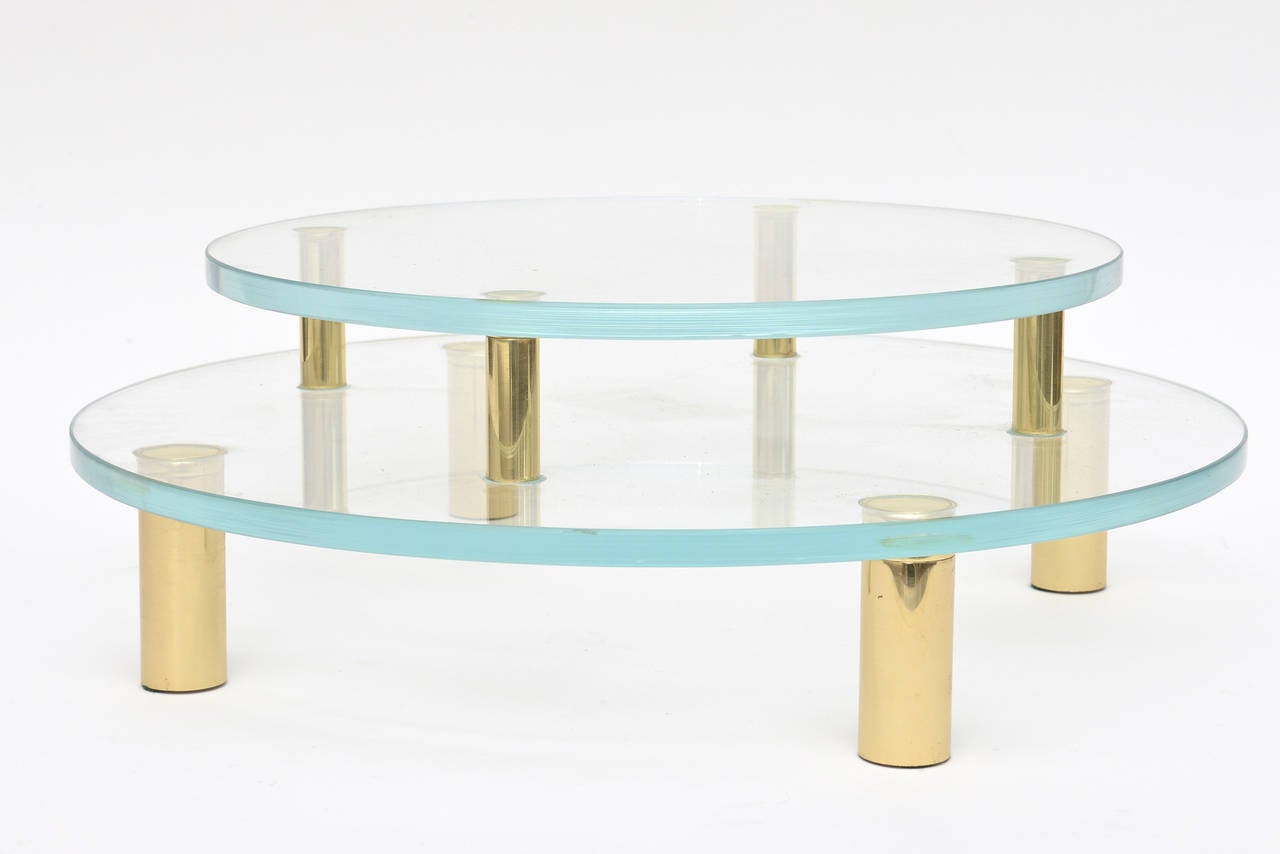 This wonderful sculptural centerpiece serving or display piece for any dining table or buffet is two-tiered. The solid brass pegs or legs attach each piece of glass. Pieces of sculpture, glass, art can be placed on this chic piece and or it can be