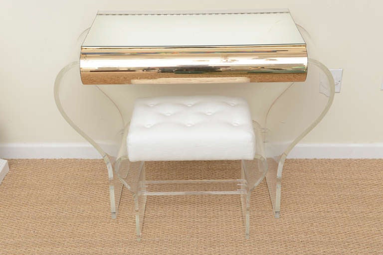 This chic lucite and mirrored vanity looks like a monemental book that has hourglass bowed sides. The mirrored top opens up with hinges to uncover a newly white lacquered interior for all your storage of makeup etc.
The rolled gold laminated front