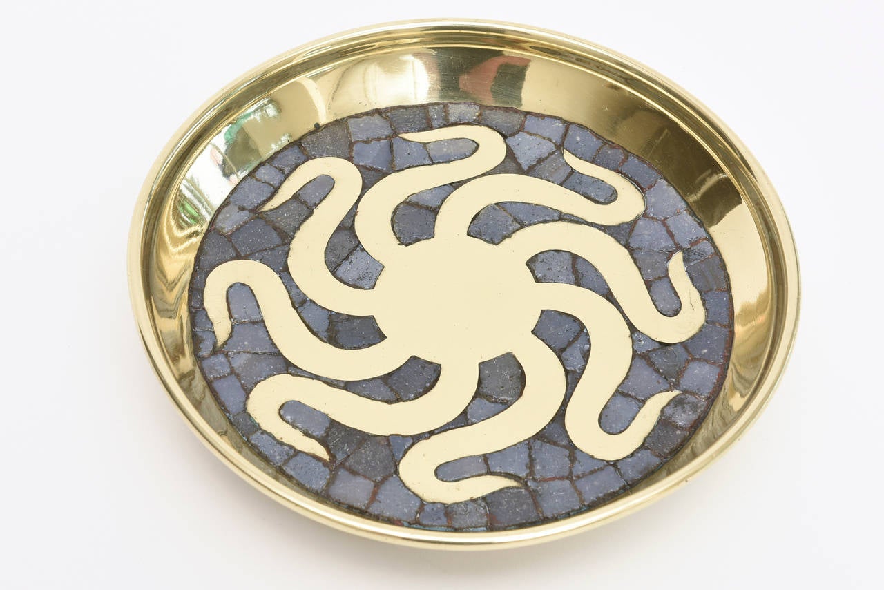 This heavy footed three-legged delightful signed and hallmarked Salvador Teran polished brass and slate blue gray glass mosaic bowl has an octopus as the design in the center in brass.
It is hallmarked with 
