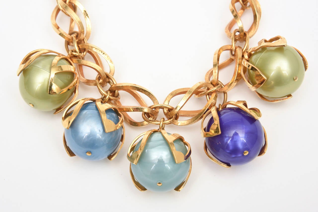 Ce collier français théâtral de Dominique Aurientis est composé de 4 grosses boules de résine qui sont enfermées dans une cage de métal doré et attachées au collier à maillons torsadés. Les 4 grosses boules aux couleurs luxuriantes de nuances