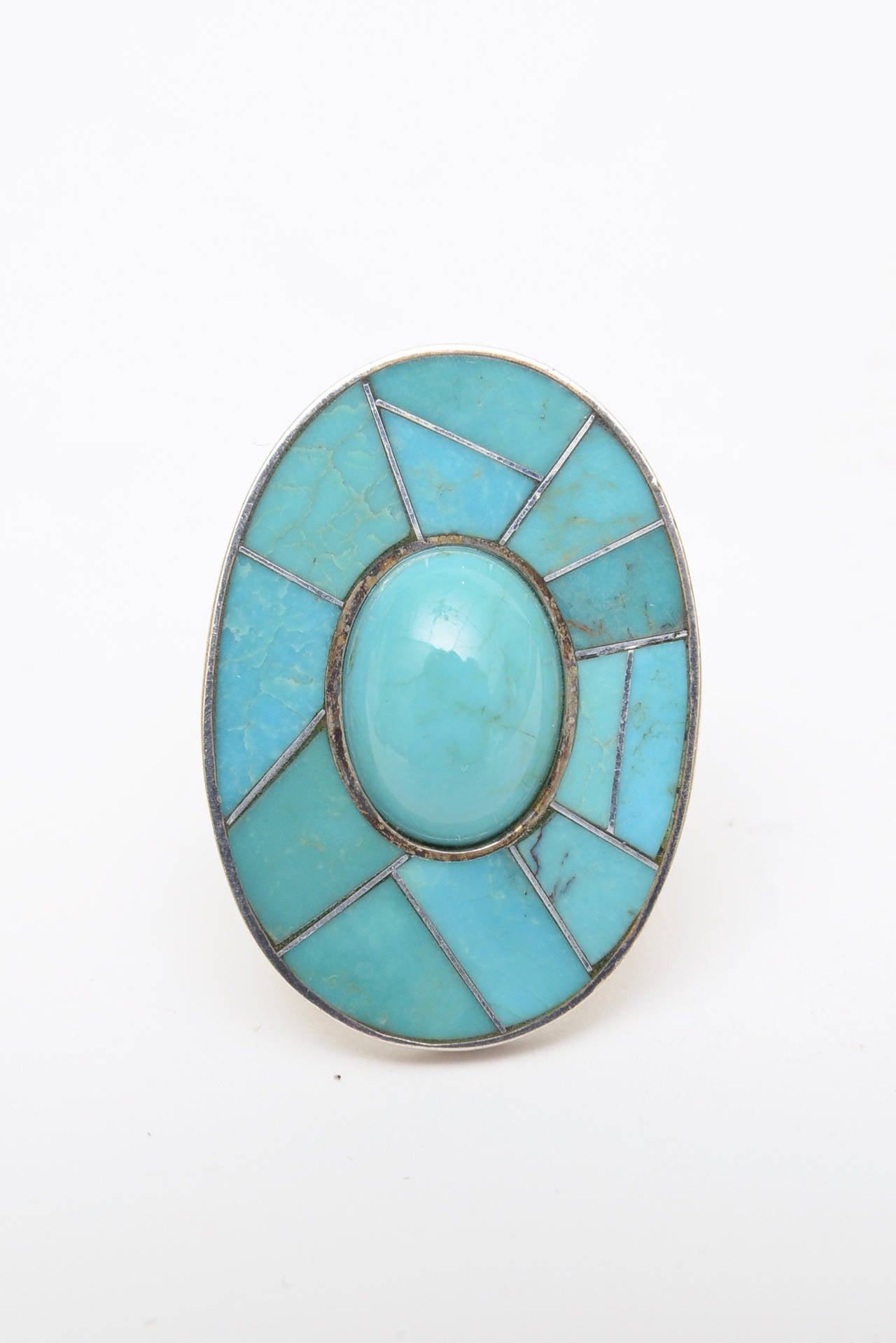 This cabochon turquoise center stone is offset like a pie with other turquoise surrounding sterling silver cross lines. This vintage ring is large and makes a great statement. This is for the woman who has a longer hand and loves dramatic jewelry