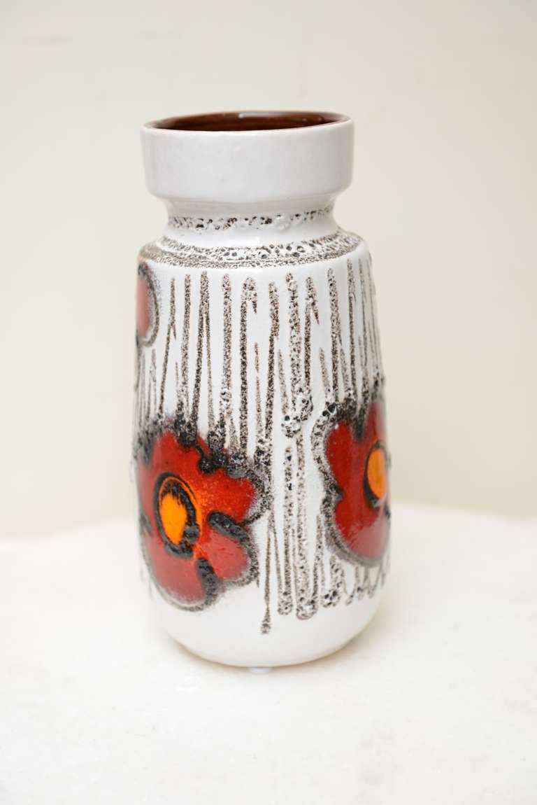 This happy drip glaze poppies vase is numbered on the bottom 242-22; west german. It has texture and great color set of against a white background black brown uneven lines draw attention to the red and orange centered poppies. The inside is a high