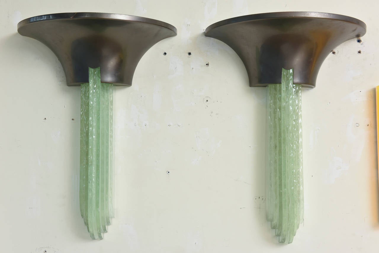 These modernist yet Art Deco revival and influenced pair of Karl Springer Purcell sconces have green colored knife edge glass graduated drops. The gun metal finish is over bronze as the tops. They are stately and dramatic.
The interior has two