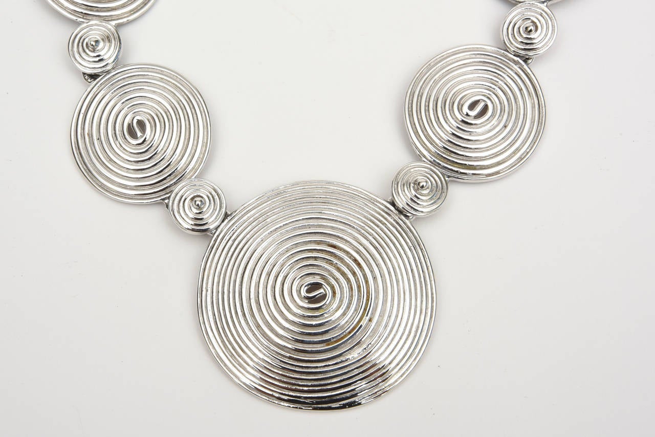 This bold statement signed Alexis Kirk vintage necklace has an influence of American Indian meets modern. The 9 spiral disks interspersed with 8 smaller disks make this very sculptural. It is from the 80's. Very conversational and very bold! This
