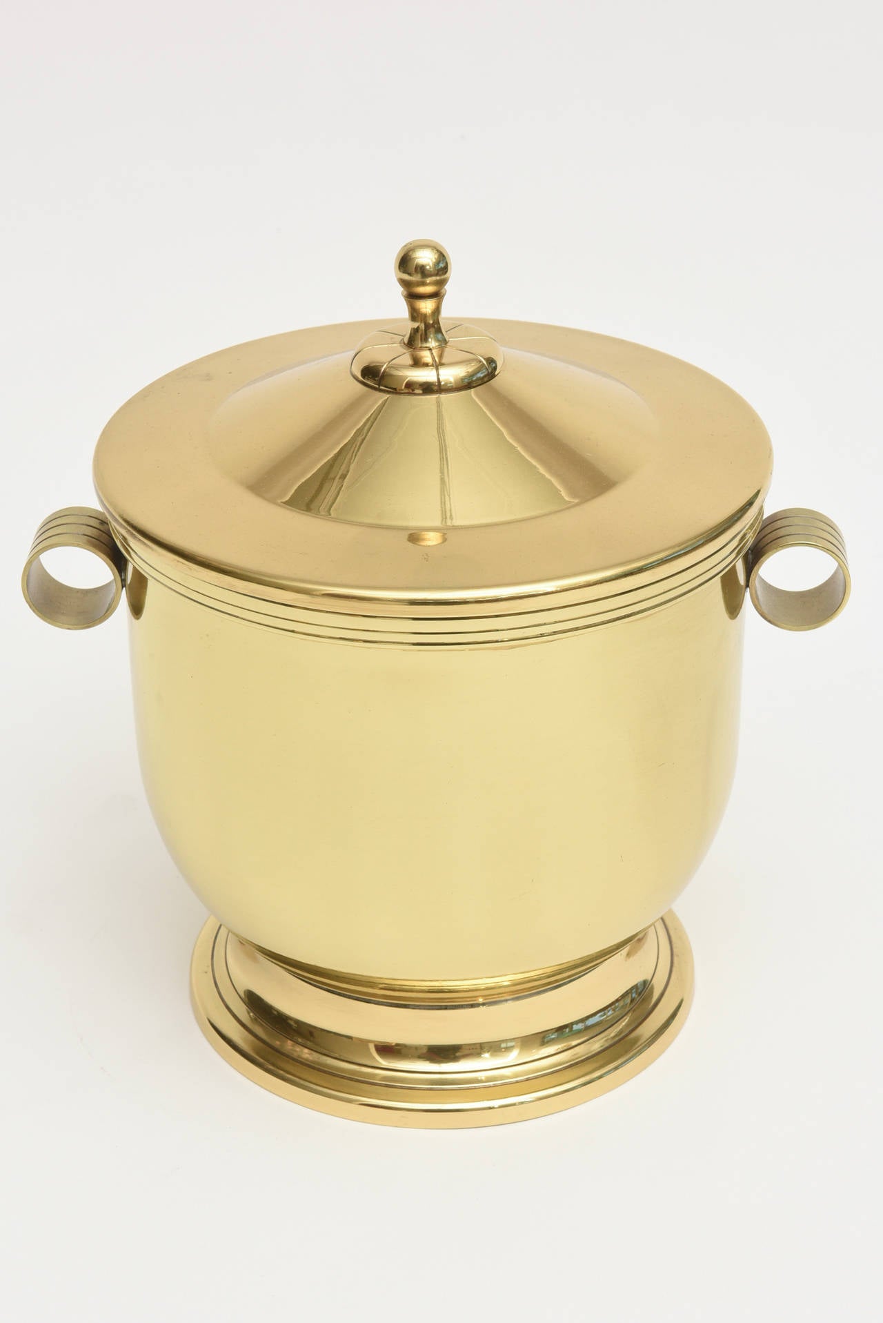 The classical lines and timelessness of this period Mid-Century Modern Tommi Parzinger polished brass and Pyrex glass liner ice bucket is forever.
It will never be dated. It is simple and elegant.
It is not signed on the bottom: The signature was