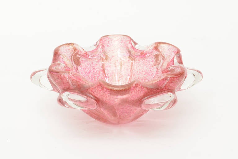 This lovely and beautiful Italian Murano glass bowl is pink with gold dust aventurine. It has 6 clear glass appendages on the outside. The scalloped folded sides add form. It goes from shades of cranberry to pink with gold. It is more vibrant in