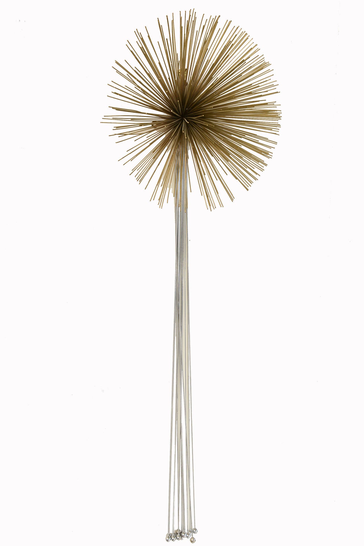This Curtis Jere wall sculpture has dangling rods ending with balls as the tips meet a starburst of brass as the pom pom. It is mixed metals with chrome at the bottom and brass at the top. This Curtis Jere vintage wall hanging sculpture can fit in