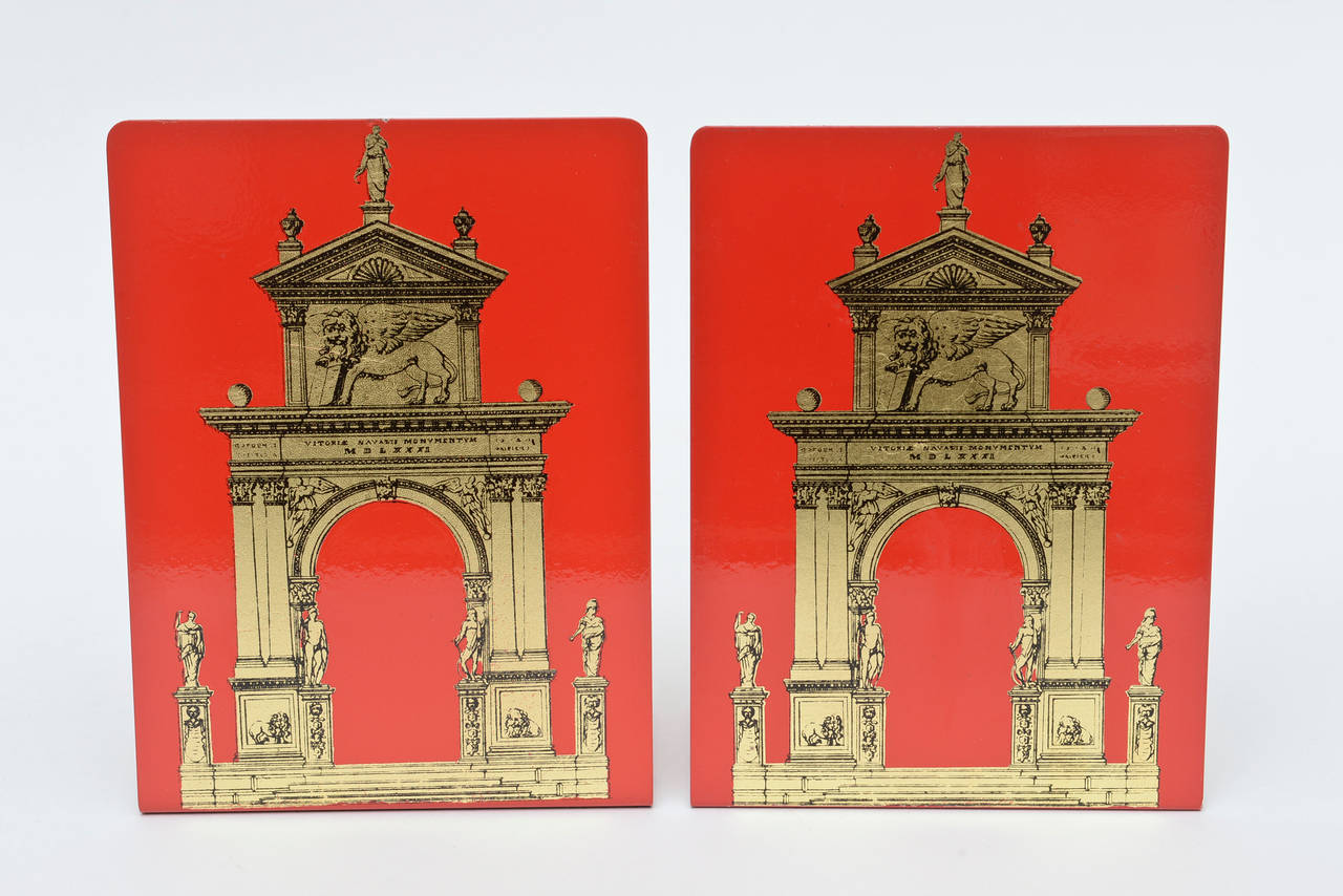 These arresting Italian Piero Fornasetti vintage metal bookends are of the Classical Roman architectural style. They are from the Porta series. The brilliant red color against gold embellishments add richness to any desk or bookcase or kitchen