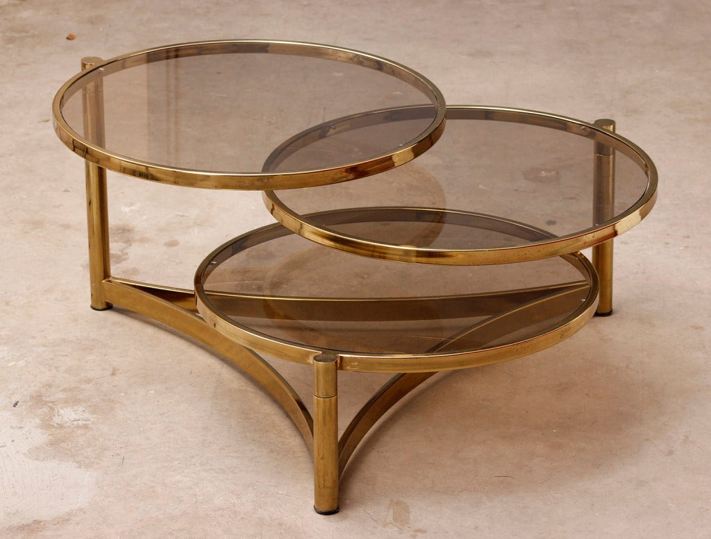 Swivel Pods in brass and glass can be reconfigured to form different shapes. 
The brass posts and frame holds three glass round tops at differing levels that can swivel to form a custom shaped table.