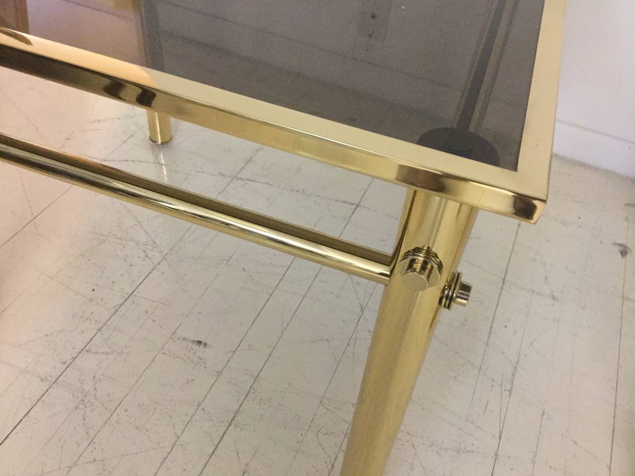 Pair of Side Tables in polished brass 
with round legs and square stretchers, 
smoked glass top.
 