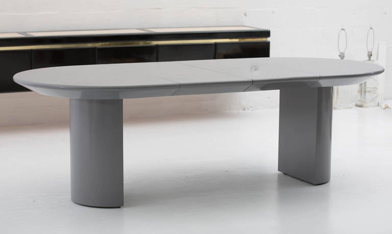Signed Dining Room Table by Karl Springer,
featuring oval top with knife edge detail
supported by two half cylinder pedestals,18"w, 9"d.
Two matching boards extend the top 
to 108"long racetrack shape,
all in dark grey lacquered piano