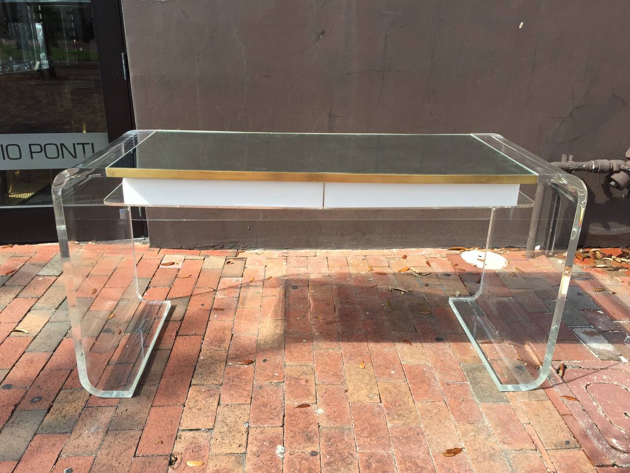 Thick clear Lucite waterfall design and white Lucite desk drawers (two), with mirror top and brass trim all around. All vintage, showing appropriate age.