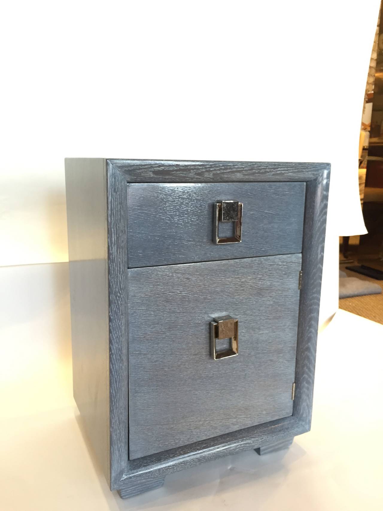 This beautiful piece is in this elegant and masculine grey cerused finish which accentuates the wood grain.

This side table has a drawer and door for storage. All hardware has been nickel-plated for that shiny finish.