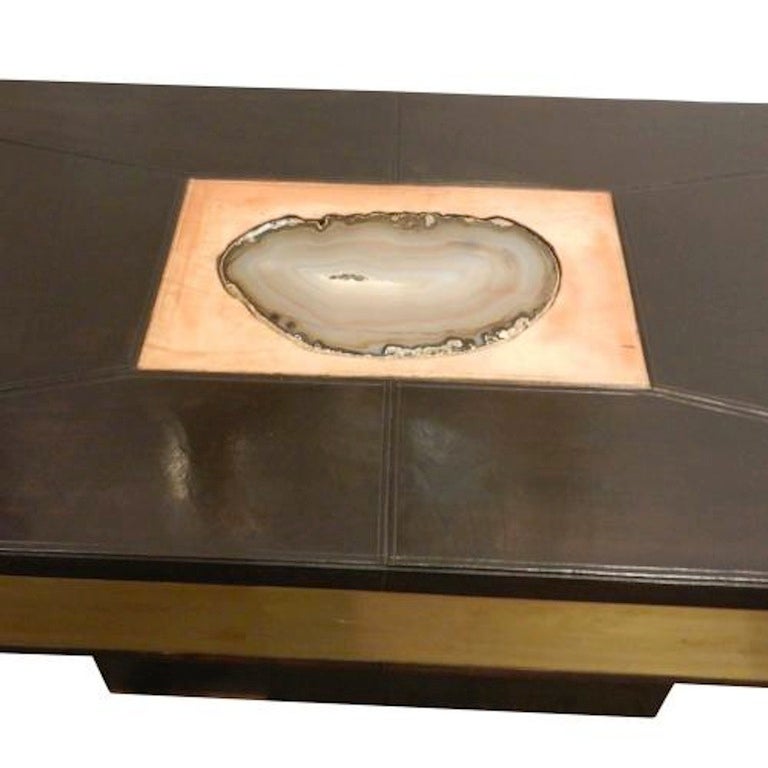 A modernist console table with a pedestal base and square, box shaped foot covered in black leather with brass panel inlays on the consoles skirt and a central large agate inlay on the consoles top which is surrounded by a natural colored leather.