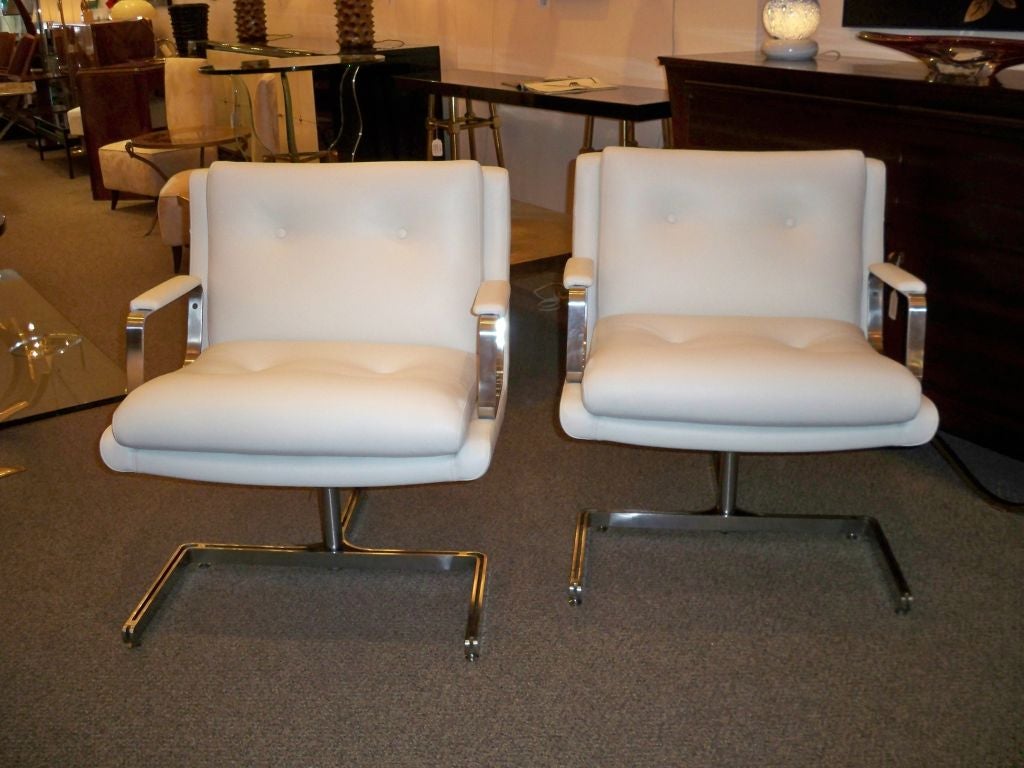 A pair of modernist club chairs each featuring a U-shaped base with extending back brace with a single pole support in chromed steel. The clubs also feature open arms, also in steel with padded, upholstered armrests, attached seat and back pillows,