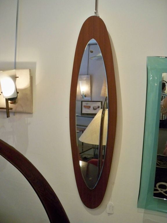 An elongated modernist wall mirror featuring a frame in teak onto which sits a central mirror, Italy, circa 1975.