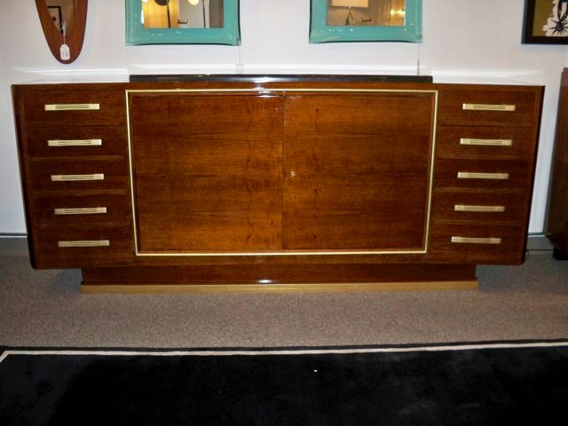 An important sideboard in Walnut featuring a concave bow shaped body which sits on a raised plinth base with a gilt bronze foot. The sideboard also features two central doors with interior shelving banded in gilt bronze which are flanked on either