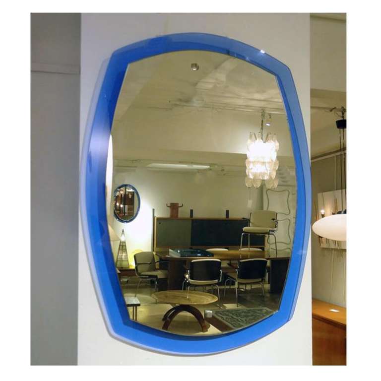 A large wall mirror featuring a rounded rectangular shaped body with a blue glass back plate which has a clear mirror mounted on top. In the style of Fontana Arte, Italy, circa 1965.