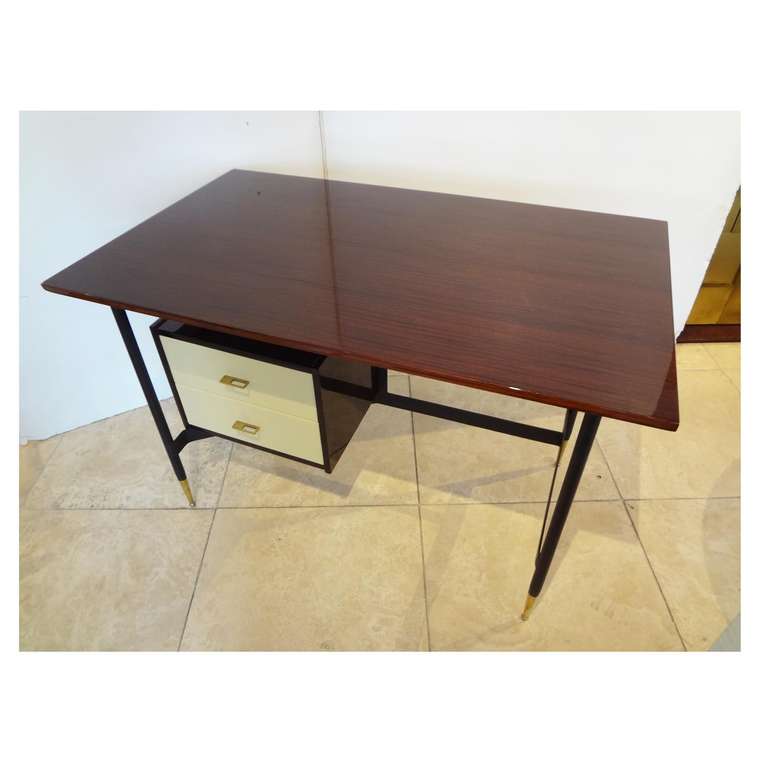 Midcentury writing desk featuring a frame in blackened metal with high polished brass sabots, two white lacquered floating drawers with a mahogany case and brass pulls and a mahogany top, Italy, circa 1955.