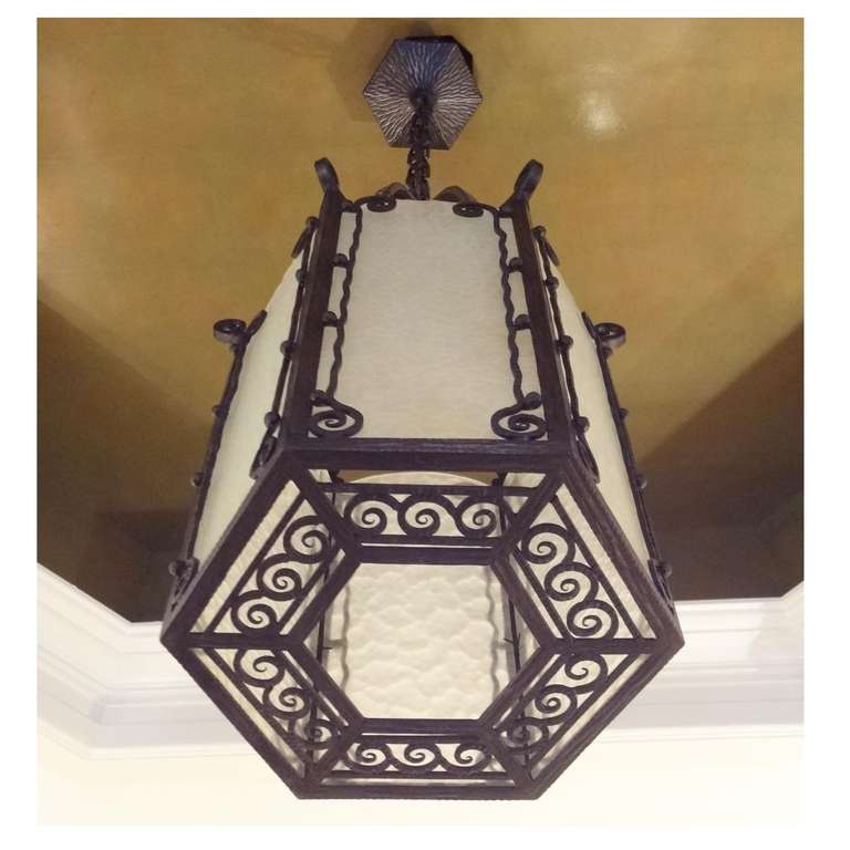 An Art Deco lantern from the Dutch Amsterdam School movement, featuring a hexagon shaped body in wrought iron with very delicately hand done scroll work and original opaque textured glass panels. The lantern has one interior light source with all