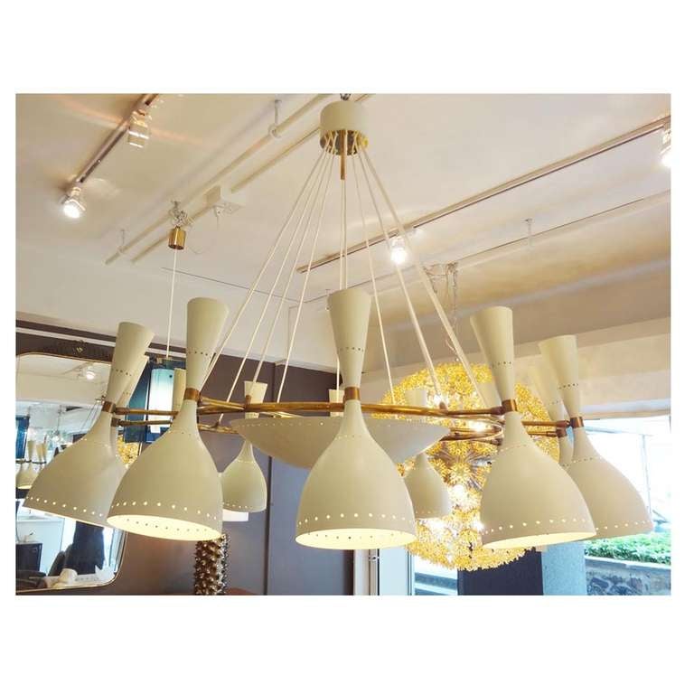 A massive scaled twelve light mid century chandelier featuring a frame in brass with twelve white wire hanging supports, twelve perforated adjustable cone shaped light diffusing shades in off white lacquered metal and an interior perforated bowl