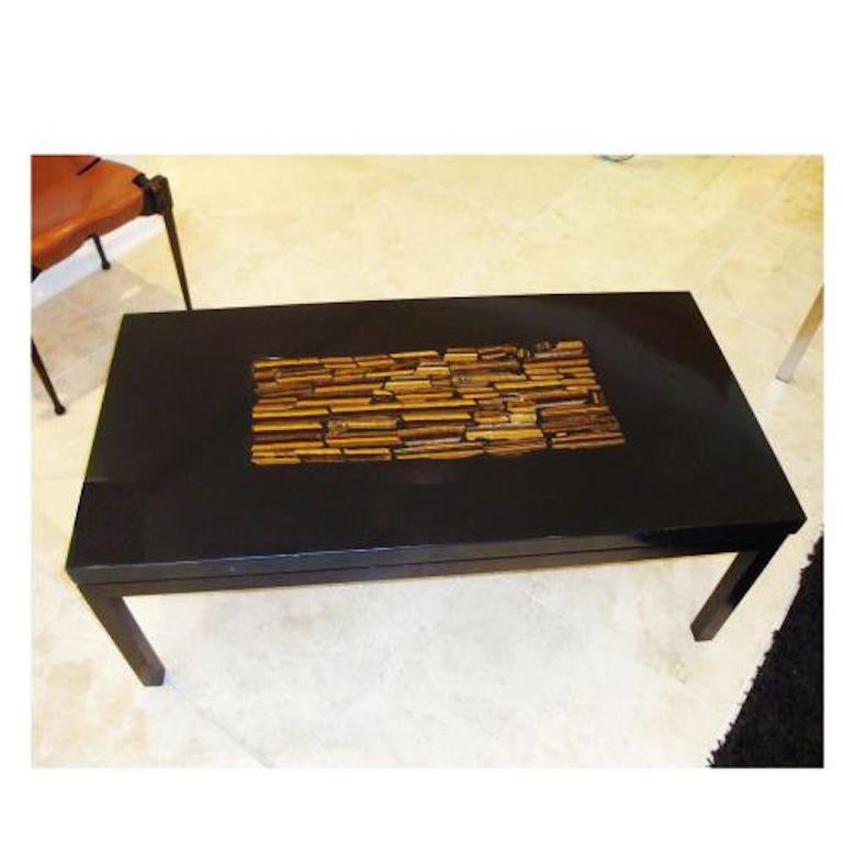 A cocktail table featuring a rectangular top in black resin with a rectangular central inlay of hand cut pieces of tigerseye in shades of gold, brown and amber. The top sits on a simple base of black painted wood with squared corner legs. The table
