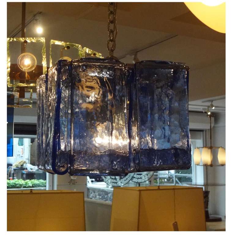 A hanging modernist fixture featuring a frame with four interior light sources in chromed steel onto which are attached multiple pieces of handmade blue / clear glass with a curling bottom. Barovier, Italy circa, 1970.