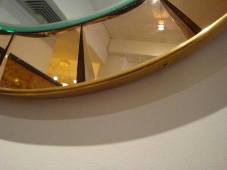 A round Mid-Century wall mirror featuring a central clear mirror with a frame of back cut amber colored mirror which is bound by brass edging. By Crystal Arte, Italy, circa 1965.