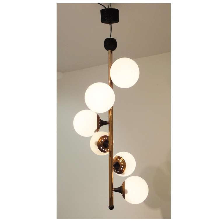 Six-light Mid-Century chandelier featuring a brass pole shaped body onto which are attached, in a swirling pattern, blackened steel and brass light sources which hold white opaque ball shaped glass light diffusing shades. The chandelier has been