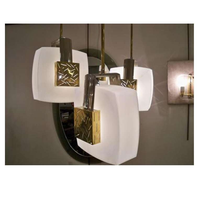A mobile shaped modernist chandelier featuring an asymmetrical shaped ceiling mount hanging system in black lacquered metal with brass accents. From this hang at various lengths, three adjustable brass poles each with a light source surrounded by a