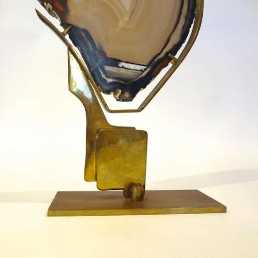 A small table sculpture featuring a piece of agate which has been mounted on a brass modernist shaped stand. In the style of Willy Daro, Belgium, circa 1970.
