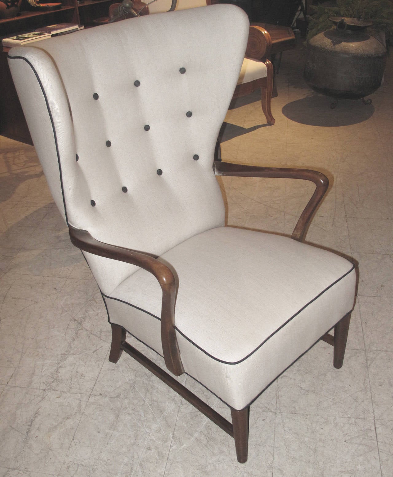 The chair newly upholstered in oatmeal colored linen with black piping and button accents.  The chair's frame of stained beech wood.