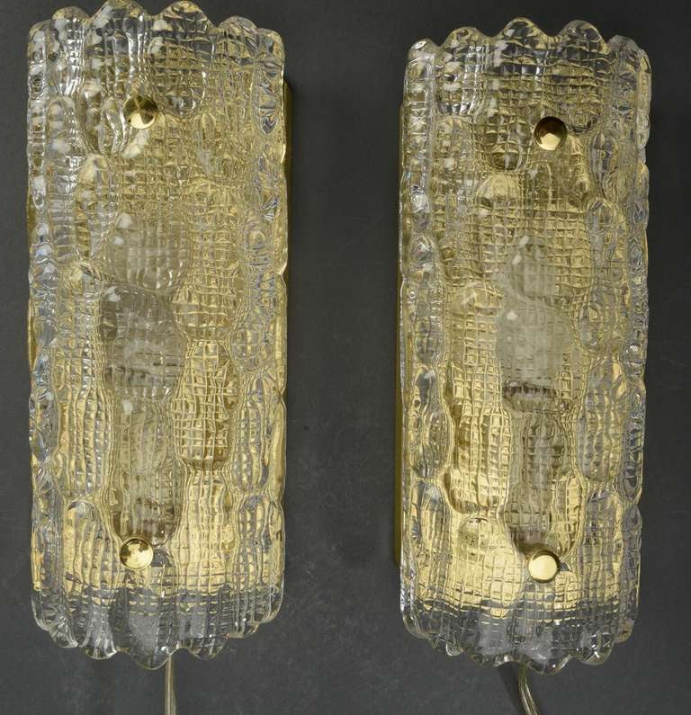Pair of 1960s pressed glass wall sconces of clear glass on brass back-plates.
The brass back-plate make the clear glass appear to have gold tones. Note:  We have more pairs of these.