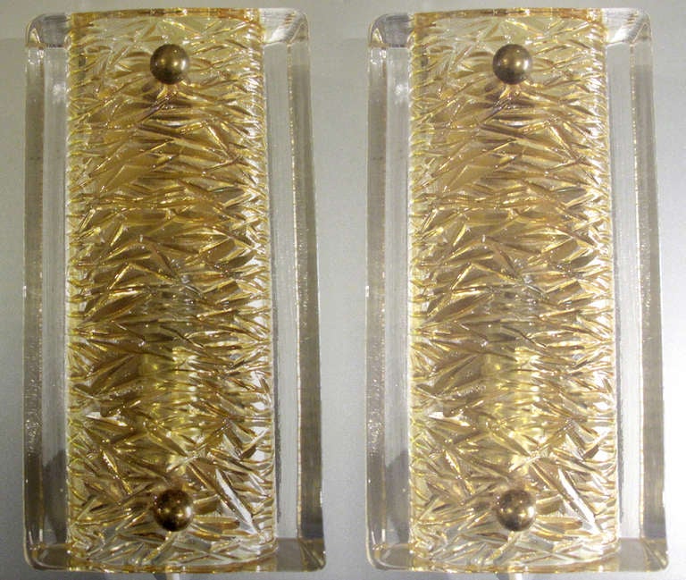 1960s wall sconces of textured gold and clear glass with brass mounts.  The sconces on brass back-plates.  Designed by Carl Fagerlund for Orrefors.