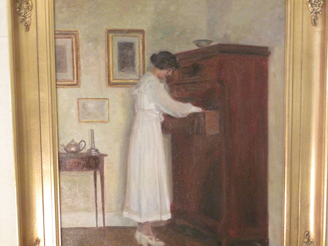 Interior scene of a woman in a white dress with an antique bureau.  Painting by Poul Friis Nybo 1869-1929.  Pupil of Zahrtman's school, studied in Paris.  Exhibited at Charlottenborg 1892-1930.  Exhibited in Chicago 1893.  Painted interiors in the