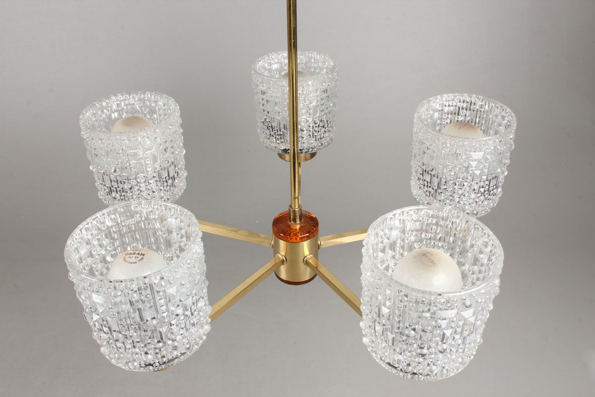 Brass and pressed glass five-arm ceiling fixture designed by Carl Fagerlund for Orrefors of Sweden, circa 1950s-early 1960s. The five arms with pressed glass shades issuing from a brass center piece mounted with amber glass. Note: Two are available.