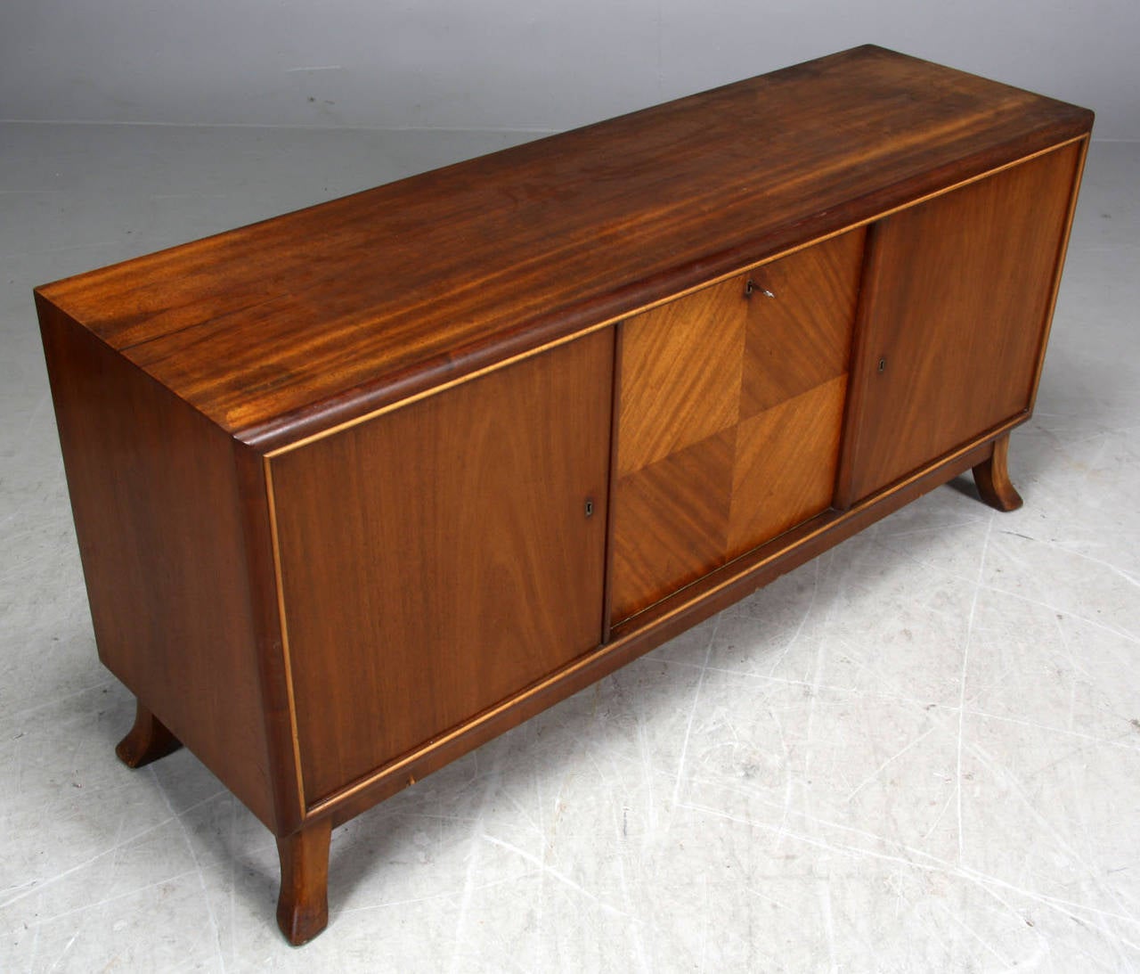 Danish cabinet maker 1940s figured mahogany sideboard/buffet. The sideboard with a decorative quarter veneered center panel. The interior fitted with drawers and shelving. The sideboard raised on four splayed legs.