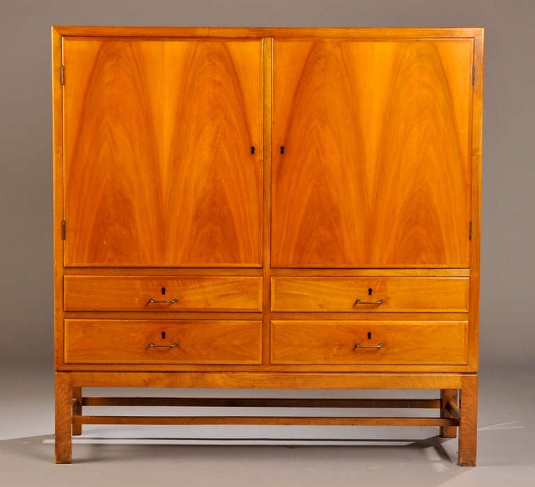 The figured walnut doors opening to a interior space fitted with shelves.  The doors above four drawers.  The whole raised on straight legs joined by stretchers.