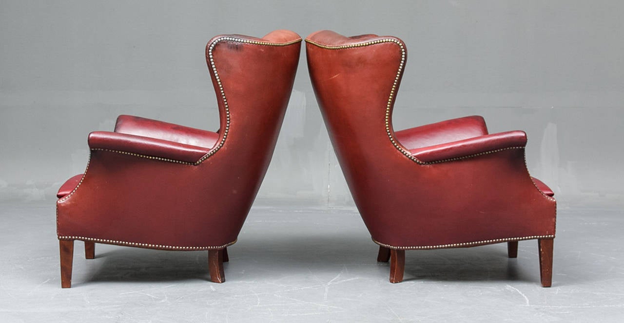 A pair of Danish 1940s wing chairs upholstered in close-nailed burgundy leather. The chairs raised on stained beech legs. The chairs attributed to Fritz Henningsen.