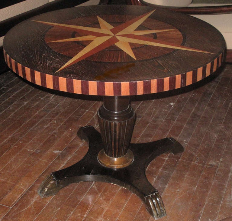 The top inlaid with exotic woods and a central nautical star design.  The table on a fluted pedestal ending on a incurved base with ribbed feet.