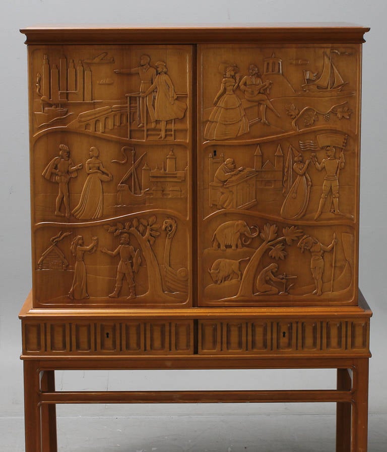 Swedish two-door walnuts cabinet, the doors carved with modern, medieval, viking and jungle scenes. The cabinet on a base with a carved frieze and joined by stretchers. The doors opening to a mahogany interior with shelving over two drawers. The