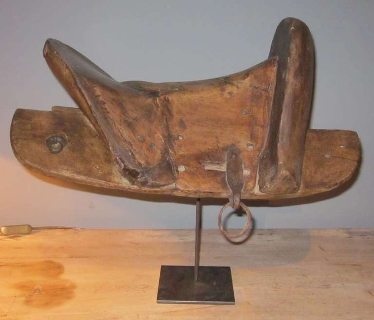 Carved wooden saddle on metal stand that makes an excellent sculpture for a table top or shelves. All hand made.