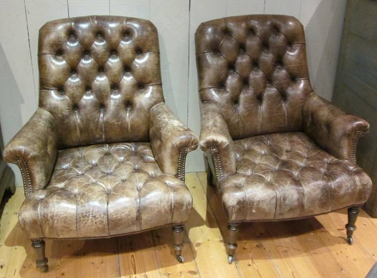 1850c English pair of brown leather all over tufted club chairs.
There are two rows of nailheads at the front of the arms.  A single row of nailheads frame the back of the chair.  
The chairs have casters. 
Amazing patina displays the time-worn