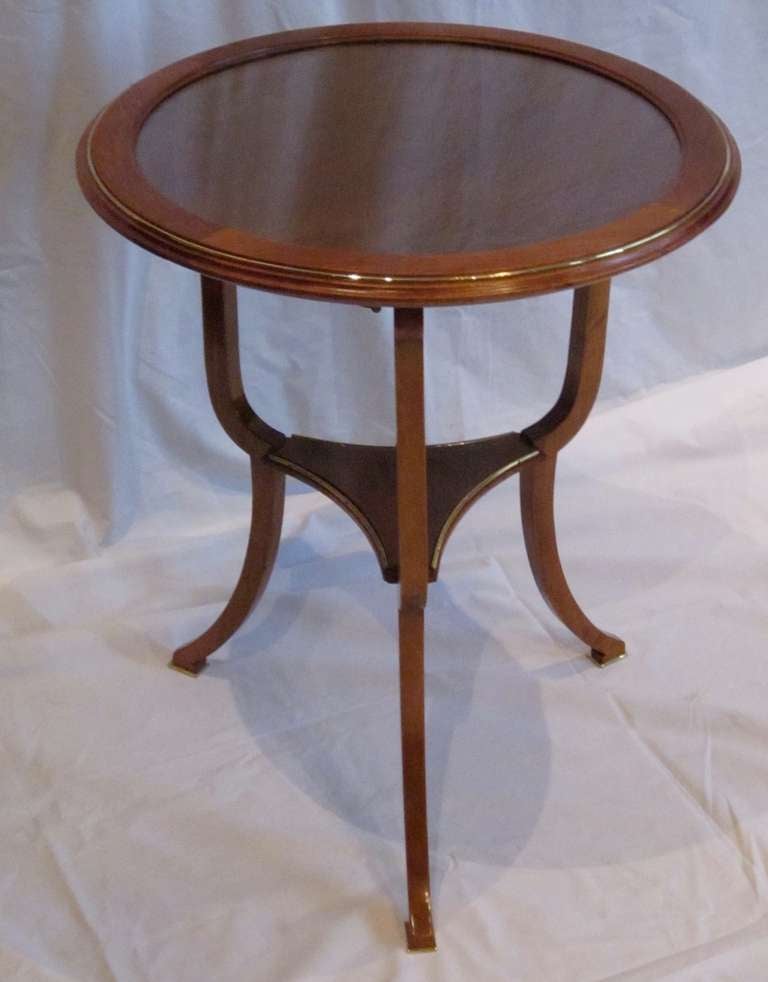 Brass trimmed two tier light brown wood side table has a framed glass top. The glass top can be lifted from the table and used as a tray, while the round wood top remains. 
Brass trims the top and curved triangle shaped second tier shelf.  The