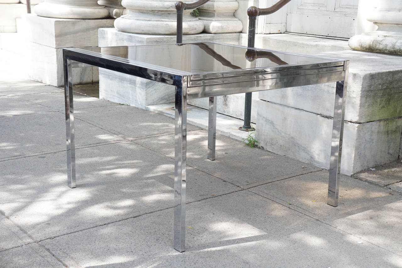 This chromed steel table with smoked glass top is perfect as a center table but opens to become an extension dining table. Designed by Milo Baughman one of this countries most adept and prolific furniture designers and lecturers. He taught at