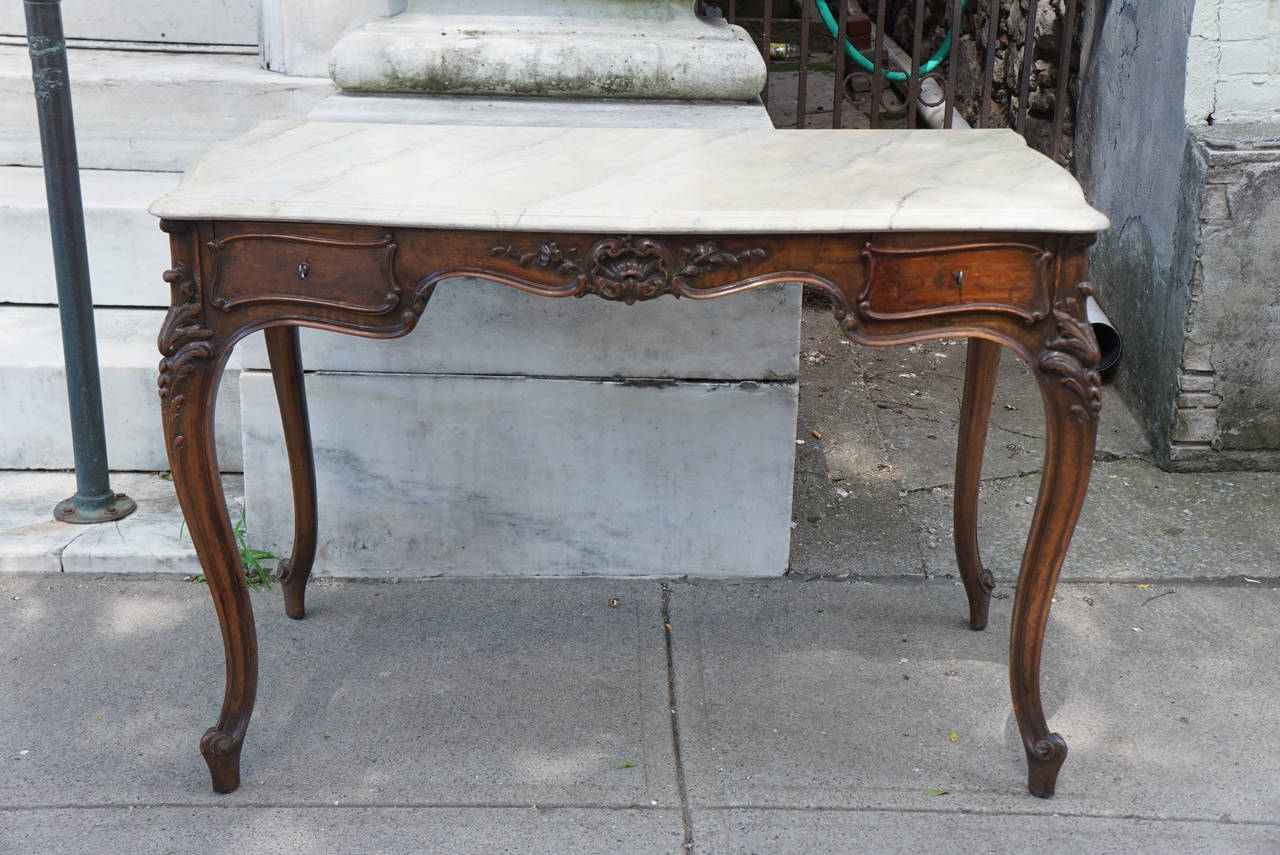 This lovely French walnut desk crafted in the Louis XV style was made, circa 1890 and retains keys to open the two drawers. The carving is bold and crisp and the interior or the drawers are lined in old wall paper. The top is marbleized and this was
