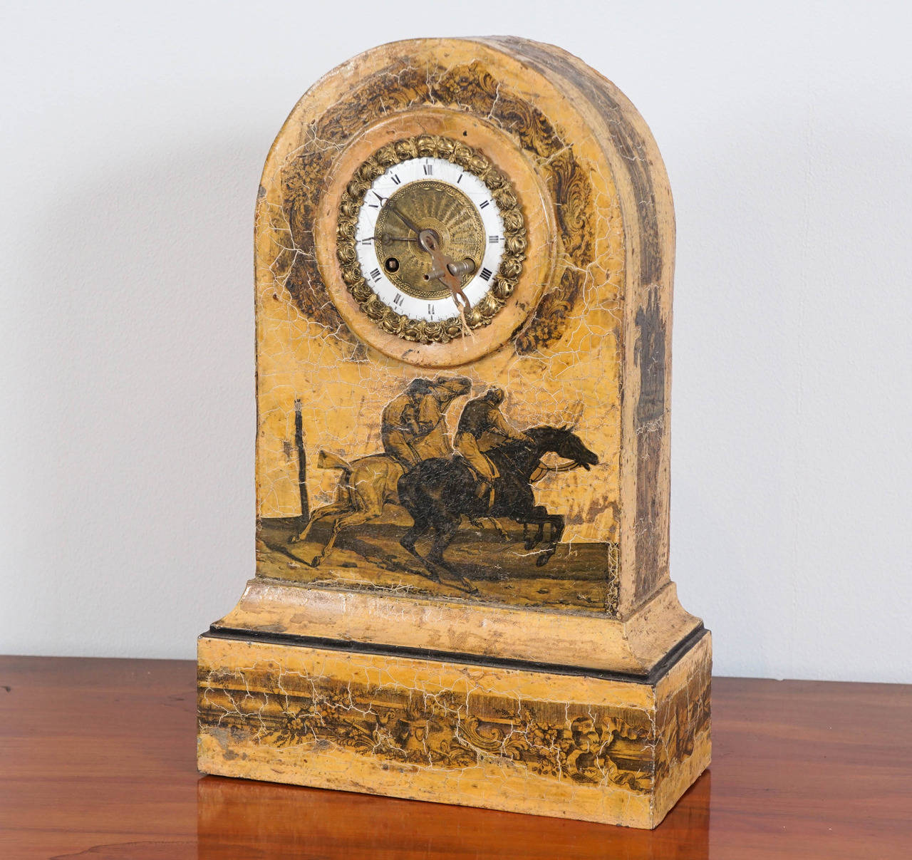 Arched Case Enclosing a White Enamel and Brass Dial. Decorated with Racing Horses and Riders. Raised on Plinth