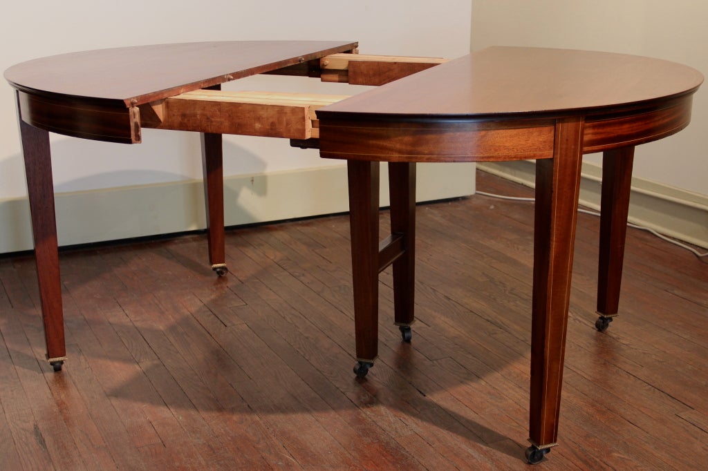 Mahogany Hepplewhite centennial dining table with accordian mechanism to take six leaves. The leaves are housed in an original wooden case. Fruitwood string inlay at edge of table, each edge of apron and legs. Casters with brass cuffs. Beautifully