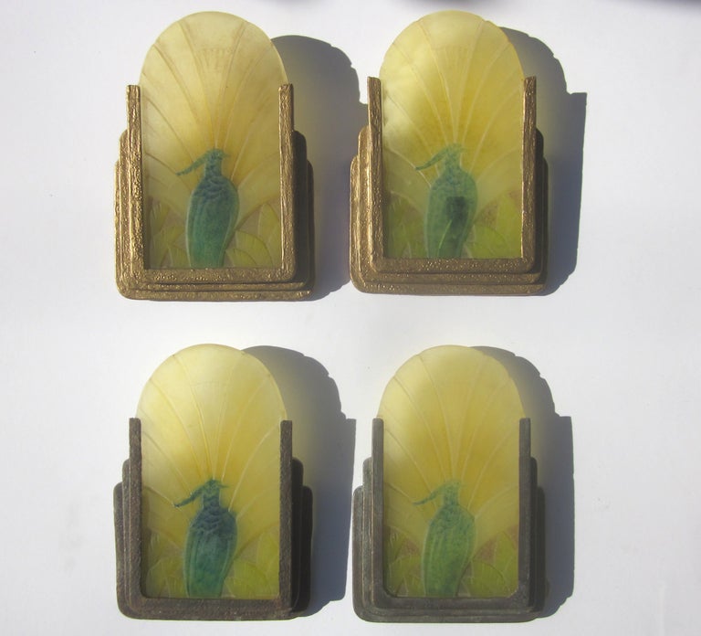 A lovely example of the fine artistry of French art glass. Each matching panel depicts a stylized fowl, surrounded by fans of fauna. The glass panel slides into stepped metal frames, lit from behind by a single bulb. There were two pairs of sconces,