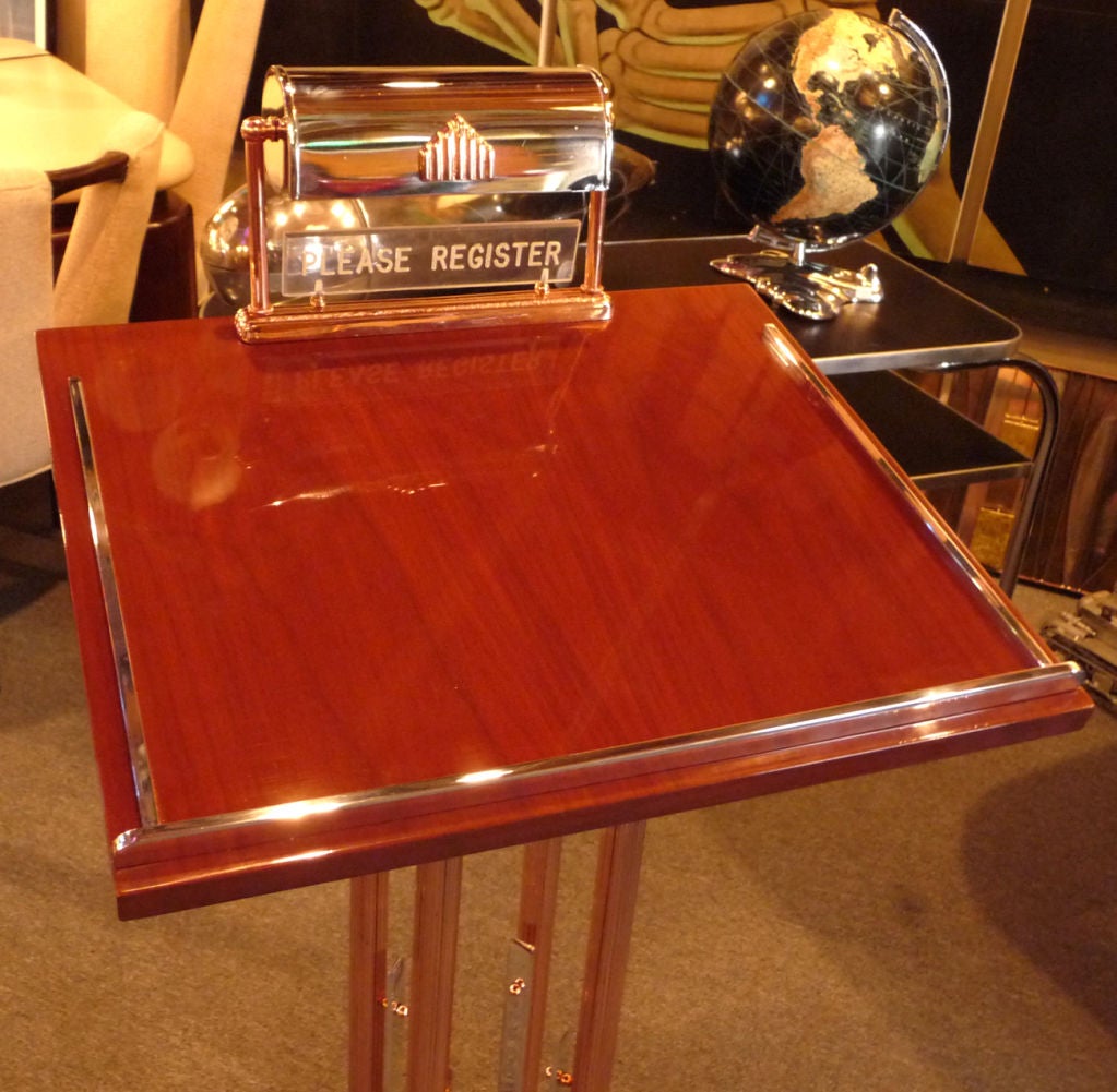 A super stylized free standing register stand in restored condition. The metals are a combination of polished aluminum and plated copper. The wooden surface is lacquered walnut. A standard lamp with turning switch illuminates the table area, and has